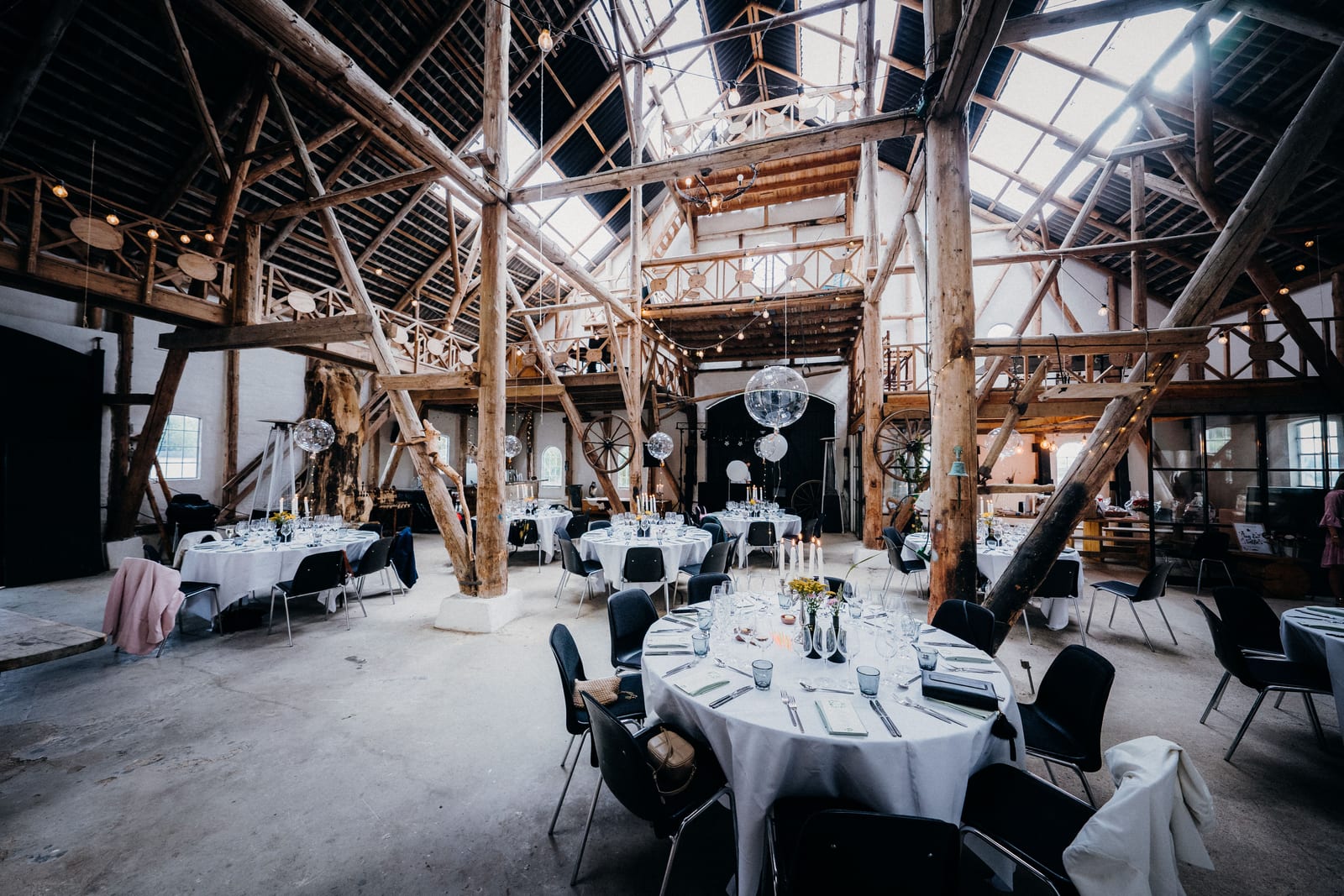 A timber-beamed hall set with round tables for an event.